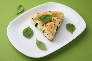 Piece of delicious puff pastry with spinach on green background