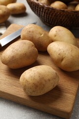 Many fresh potatoes, board and knife on grey table, closeup