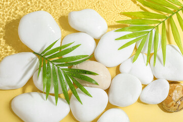 Spa stones and palm leaves in water on yellow background, flat lay