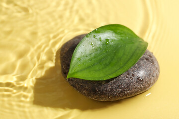 Spa stone and green leaf on yellow background, closeup