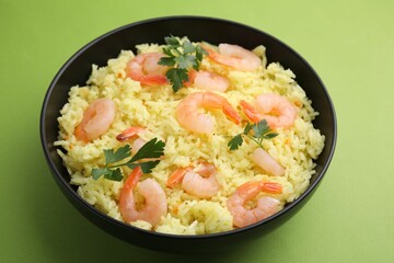 Delicious risotto with shrimps and parsley in bowl on light green background, closeup