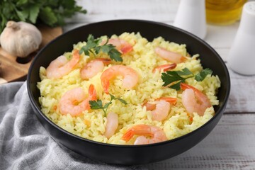 Delicious risotto with shrimps and parsley in bowl on white wooden table, closeup