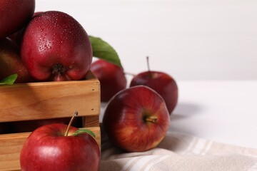 Fresh red apples in wooden crate on white table, closeup. Space for text