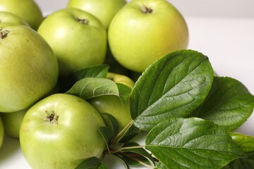 Fresh ripe green apples with leaves on white table, closeup