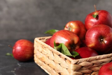 Fresh red apples and leaves in basket on dark grey table, closeup. Space for text