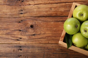 Fresh ripe green apples in crate on wooden table, top view. Space for text