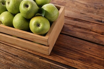 Fresh ripe green apples with water drops in crate on wooden table. Space for text