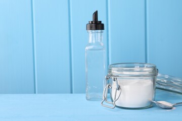 Natural cleaning products. Vinegar in bottle, baking soda and spoon on light blue wooden table....
