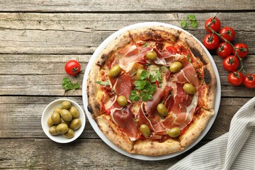 Tasty pizza with cured ham, olives, tomatoes and parsley on wooden table, top view