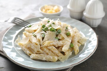 Delicious pasta with green peas, cheese and creamy sauce on grey table, closeup