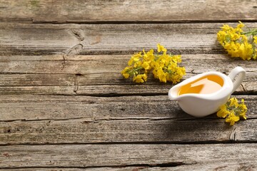 Rapeseed oil in gravy boat and beautiful yellow flowers on wooden table, space for text