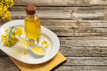 Rapeseed oil in glass bottle, gravy boat and beautiful yellow flowers on wooden table, space for...