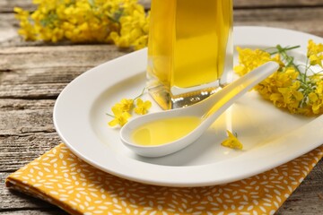 Rapeseed oil in gravy boat, bottle and beautiful yellow flowers on wooden table, closeup