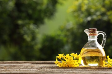 Rapeseed oil in glass jug and beautiful yellow flowers on wooden table outdoors, space for text