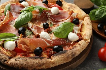 Tasty pizza with cured ham, olives, mozzarella cheese, sun-dried tomato and arugula on table,...