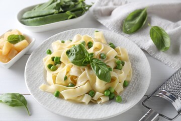 Delicious pasta with green peas and fresh basil on white wooden table