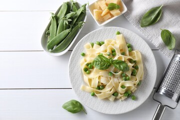 Delicious pasta with green peas and fresh basil on white wooden table, flat lay. Space for text
