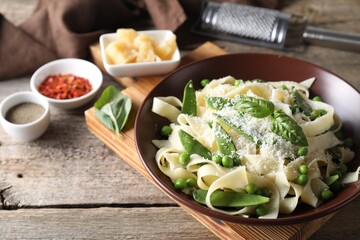 Delicious pasta with green peas, fresh basil and cheese on wooden table, closeup