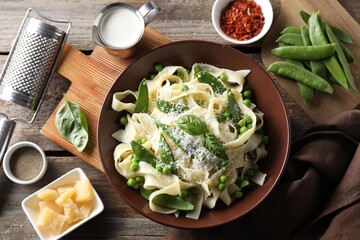 Delicious pasta with green peas and ingredients on wooden table, flat lay