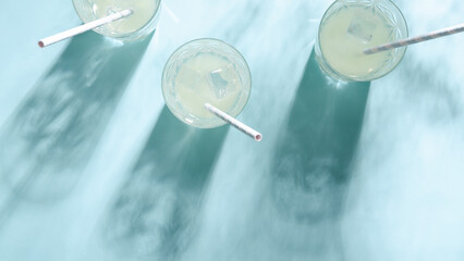 Three glasses of lemonade with straw on blue background.