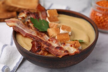 Delicious lentil soup with bacon and parsley in bowl on light table, closeup
