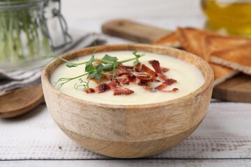Delicious potato soup with bacon and microgreens in bowl on wooden table, closeup