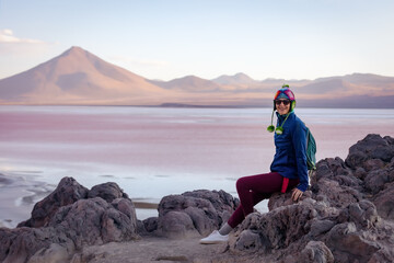 A girl in a hat sits on a large stone against the background of the Colorado Lagoon. Bolivia
