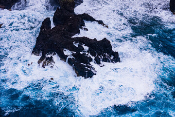 Aerial view of big waves crashing into cliffs near the ocean shore of Madeira island