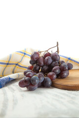 Cutting board with bunch of organic black grapes on white wooden background..