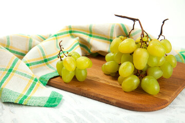 Cutting board with bunch of organic green grapes on white wooden background..