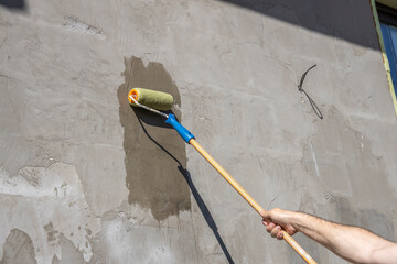A man applies primer to a concrete wall using a roller. The image shows the process of painting...