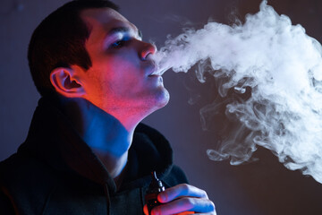 A man exhales a cloud of steam from an electronic cigarette. Vape pod mod , close-up . Colored neon...