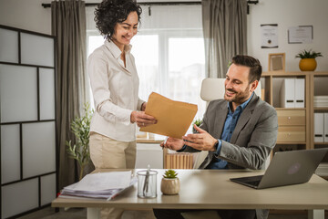 Two excited colleagues open envelope with documents at office