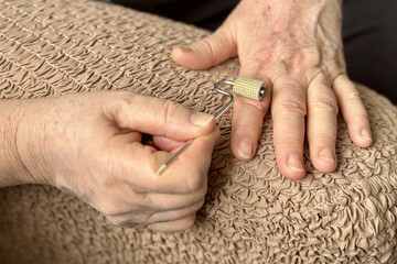 An unknown elderly woman sitting in an armchair makes herself a hand massage with her hand with a...