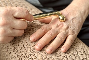 An unknown elderly woman sitting in an armchair makes herself a hand massage with her hand with a...
