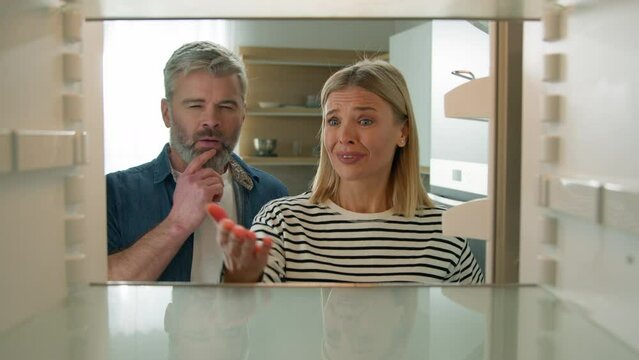 Point of view POV from inside refrigerator adult middle-aged family couple woman man senior mature husband wife open empty fridge confused come up with idea order food delivery app using mobile phone