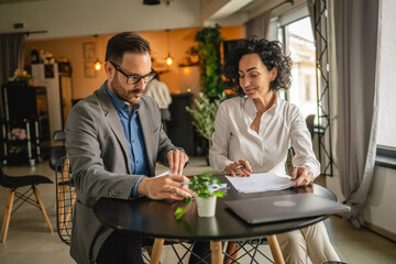 Man and woman colleagues hold documents and work together at cafe