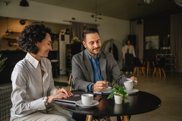 Two colleagues man and woman on break at cafe drink coffee and talk