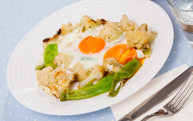 Plate of tasty fried eggs with cauliflower, green beans and condiment