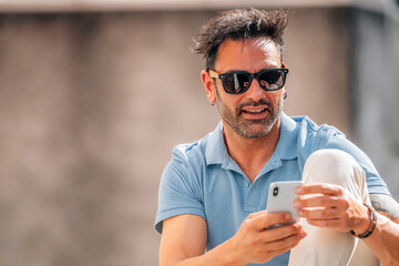 attractive young man with sunglasses looking at his mobile phone on the street outdoors