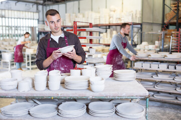 Focused pottery expert in maroon apron meticulously inspecting quality of freshly produced handmade...