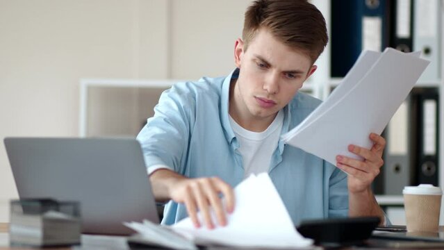 Worried businessman searching important documents files or information in heap of papers on worktable in home office