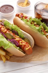 Delicious hot dogs with lettuce, onion and pickle on white wooden table, closeup