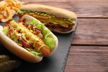 Delicious hot dogs with lettuce, onion and pickle on wooden table. Space for text