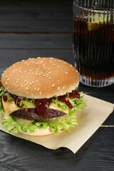 Burger with delicious patty and soda drink on black wooden table