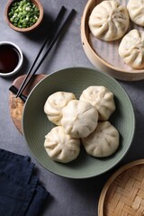 Delicious bao buns (baozi), chopsticks, soy sauce and green onion on grey table, flat lay