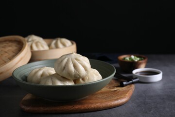 Delicious bao buns (baozi) in bowl on grey textured table, closeup
