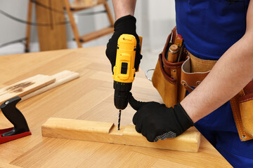 Young worker using electric drill at table in workshop, closeup