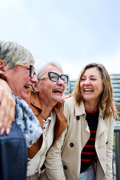 Vertical. Group of three mature caucasian women enjoying embracing walk together laughing outdoor. Senior female friend having fun hugging strolling happy urban city street. Elderly people golden ager