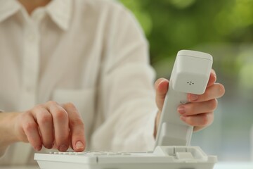 Assistant dialing number on telephone against blurred background, closeup